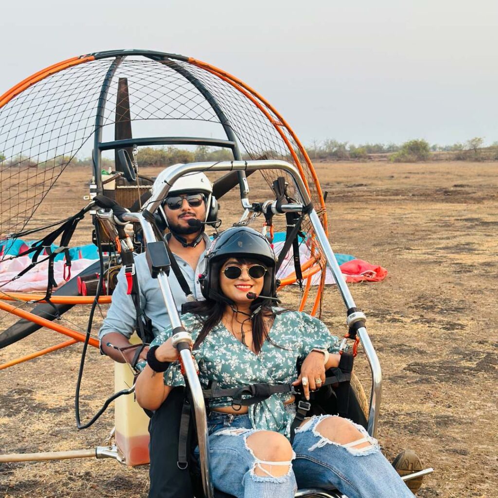 A tandem paramotor flying over the picturesque coastline of Goa with clear blue skies and lush greenery below