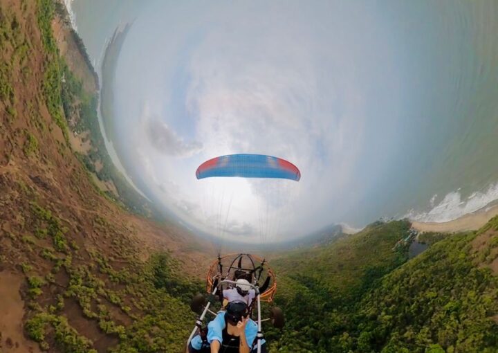 Paramotoring adventure in Goa: A paramotor glides above a serene coastline with palm trees and the Arabian Sea, capturing the essence of adventure sports in Goa.