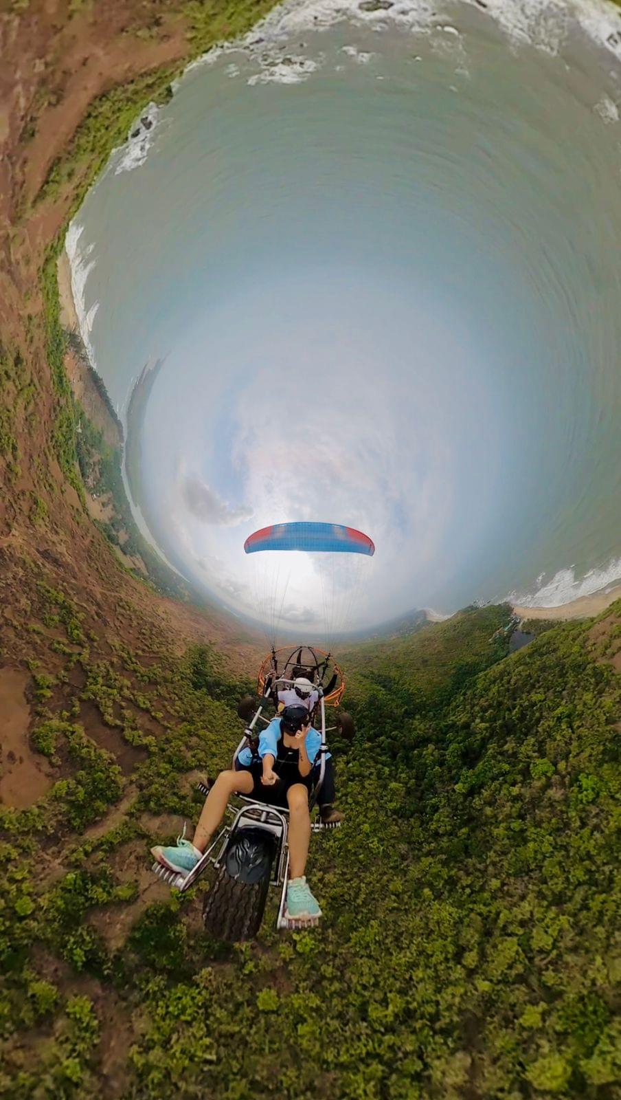 Paramotoring adventure in Goa: A paramotor glides above a serene coastline with palm trees and the Arabian Sea, capturing the essence of adventure sports in Goa.